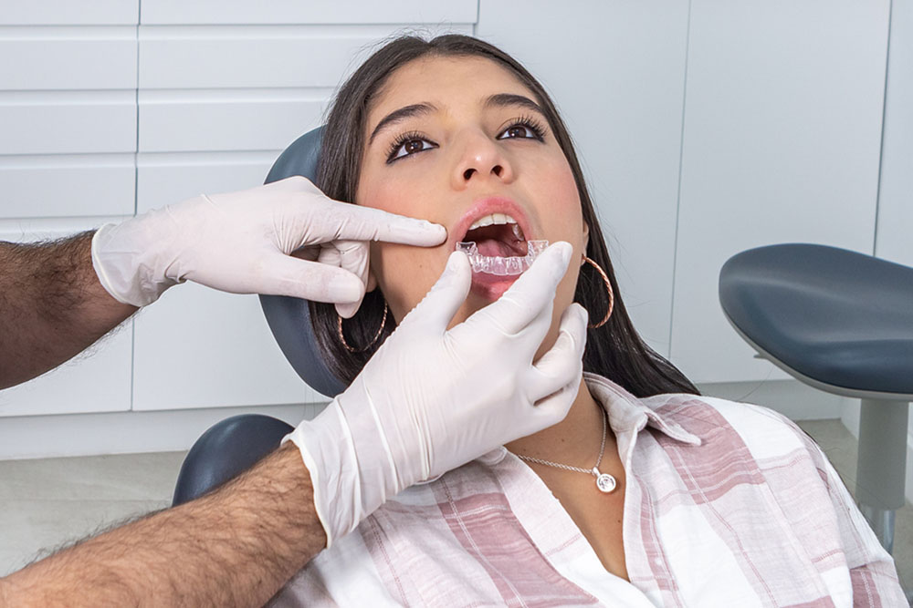 Professional male orthodontist applying retainer on teeth of female patient
